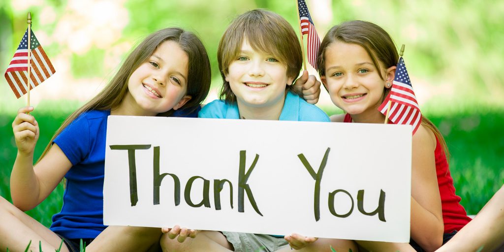 three smiling children waving flags and holding up a 'thank you' sign