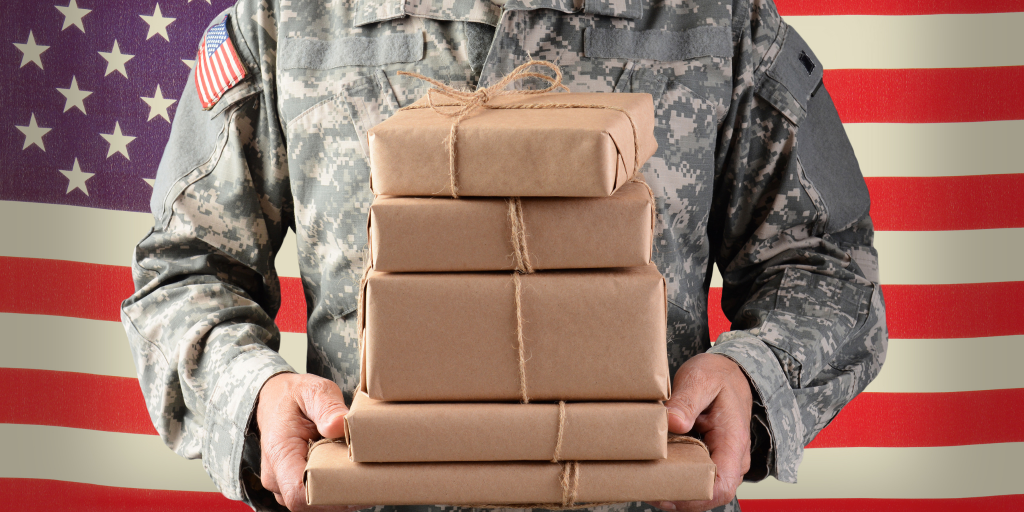 Closeup of someone in a military uniform standing in front of American flag holding several packages wrapped in kraft paper.