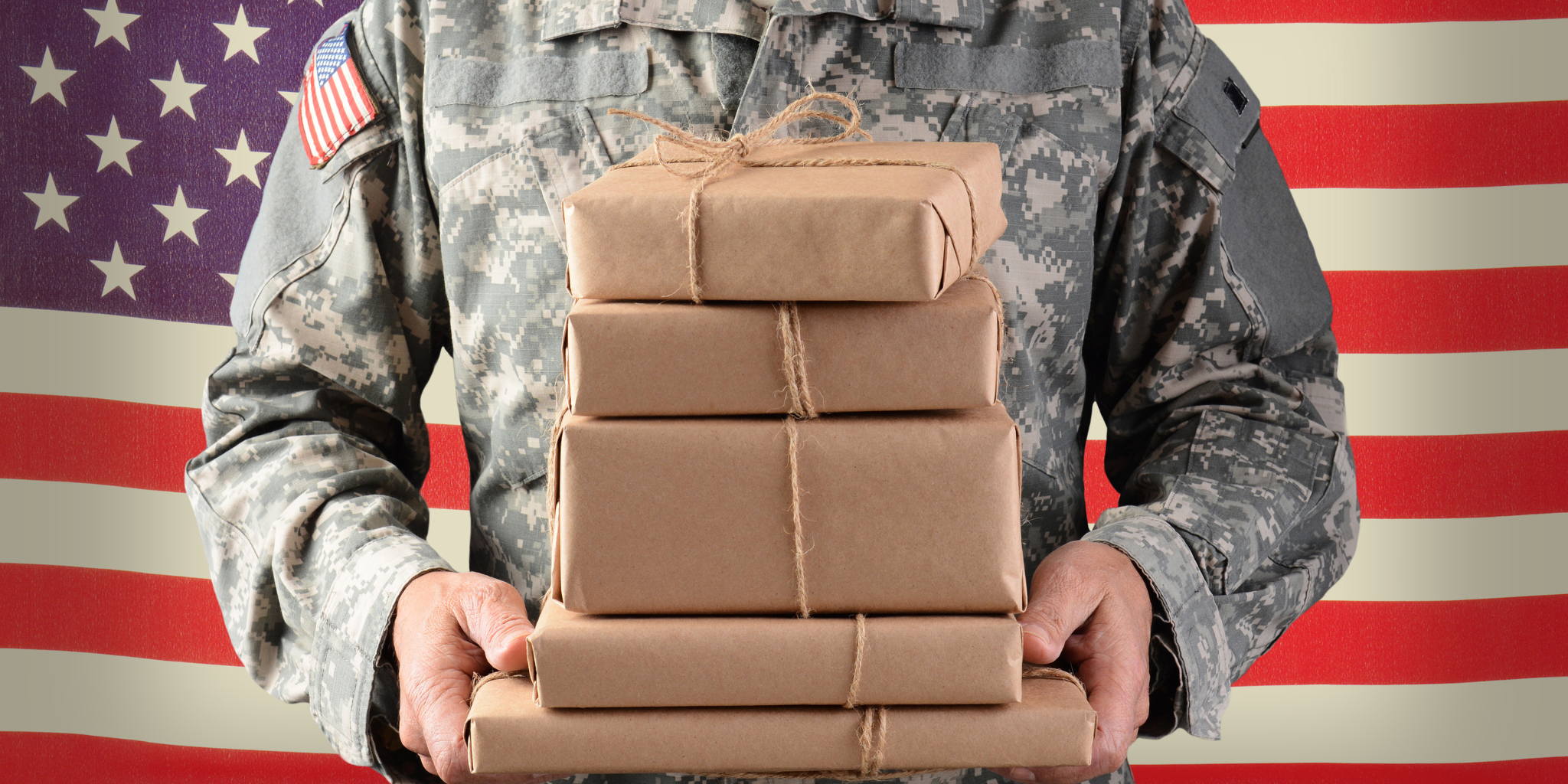 Closeup of someone in a military uniform standing in front of American flag holding several packages wrapped in kraft paper.