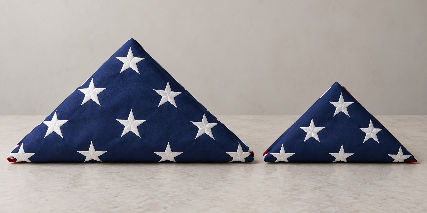 Folded 5 by 9.5 foot burial flag beside a folded 3 by 5 foot flag showing the size difference